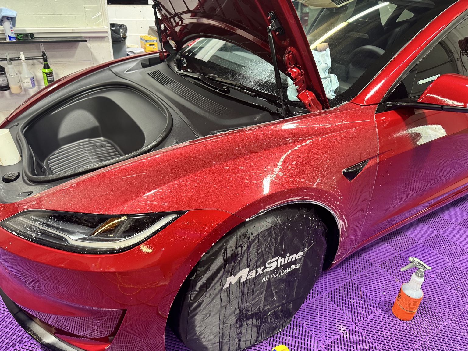 Red Tesla Model 3 front fender, bumper and headlight during PPF installation, with the hood open and front wheel protected