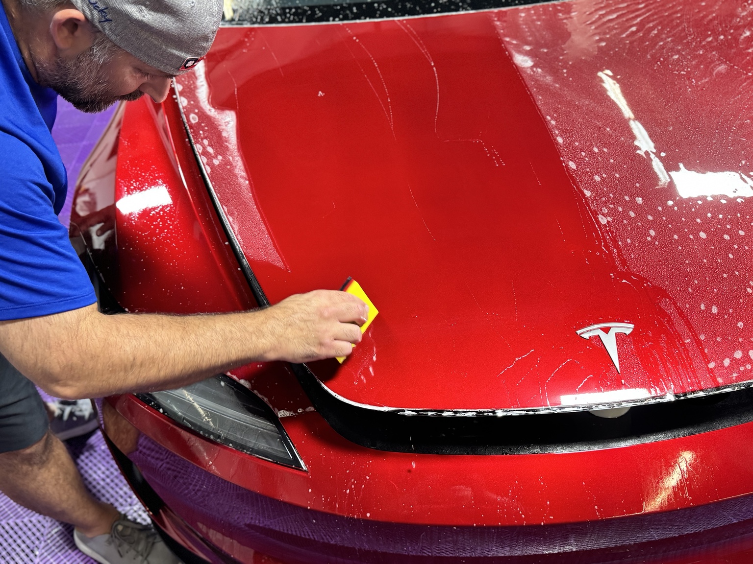 Kris Shuman squeegeeing clear paint protection film onto the full hood of a red Tesla Model 3 at STL Auto Defenders in Arnold