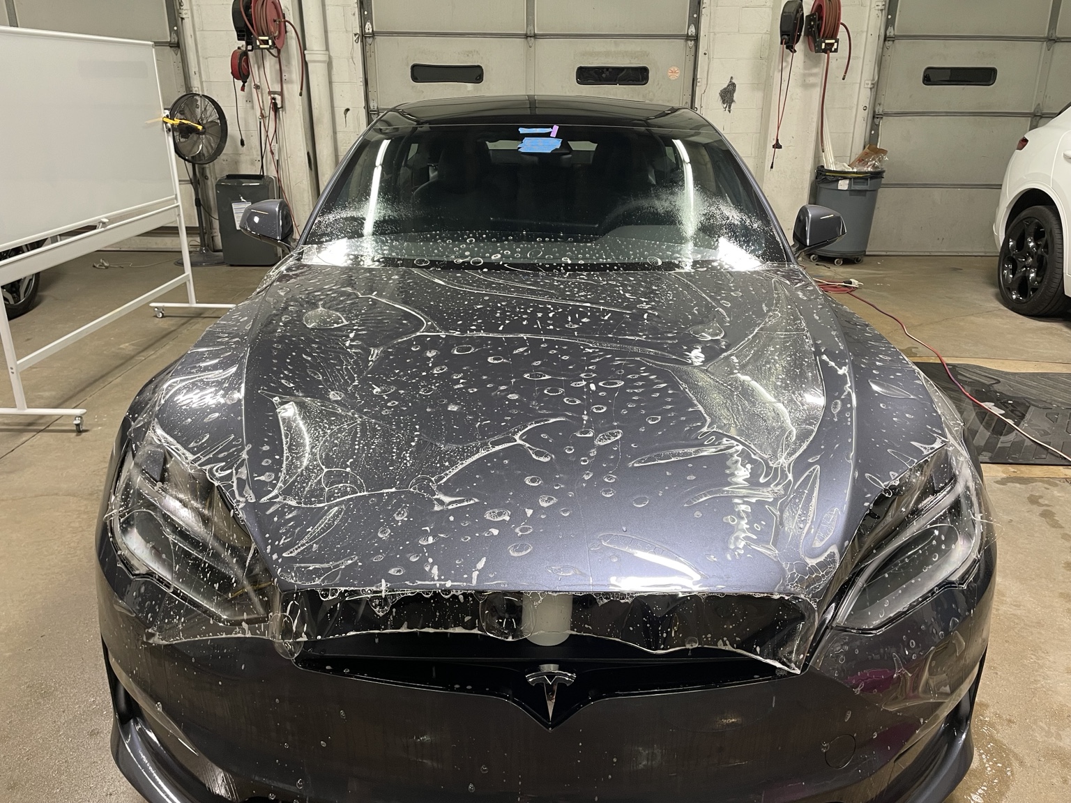 Clear paint protection film positioned across the full Tesla Plaid hood during installation