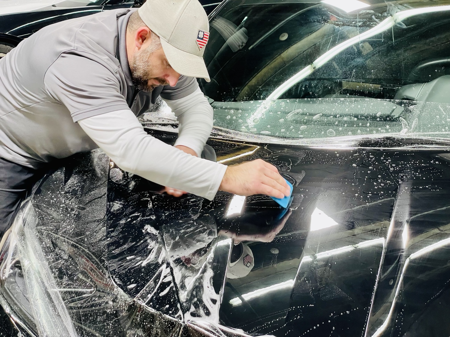 Owner squeegeeing clear PPF onto a black vehicle hood