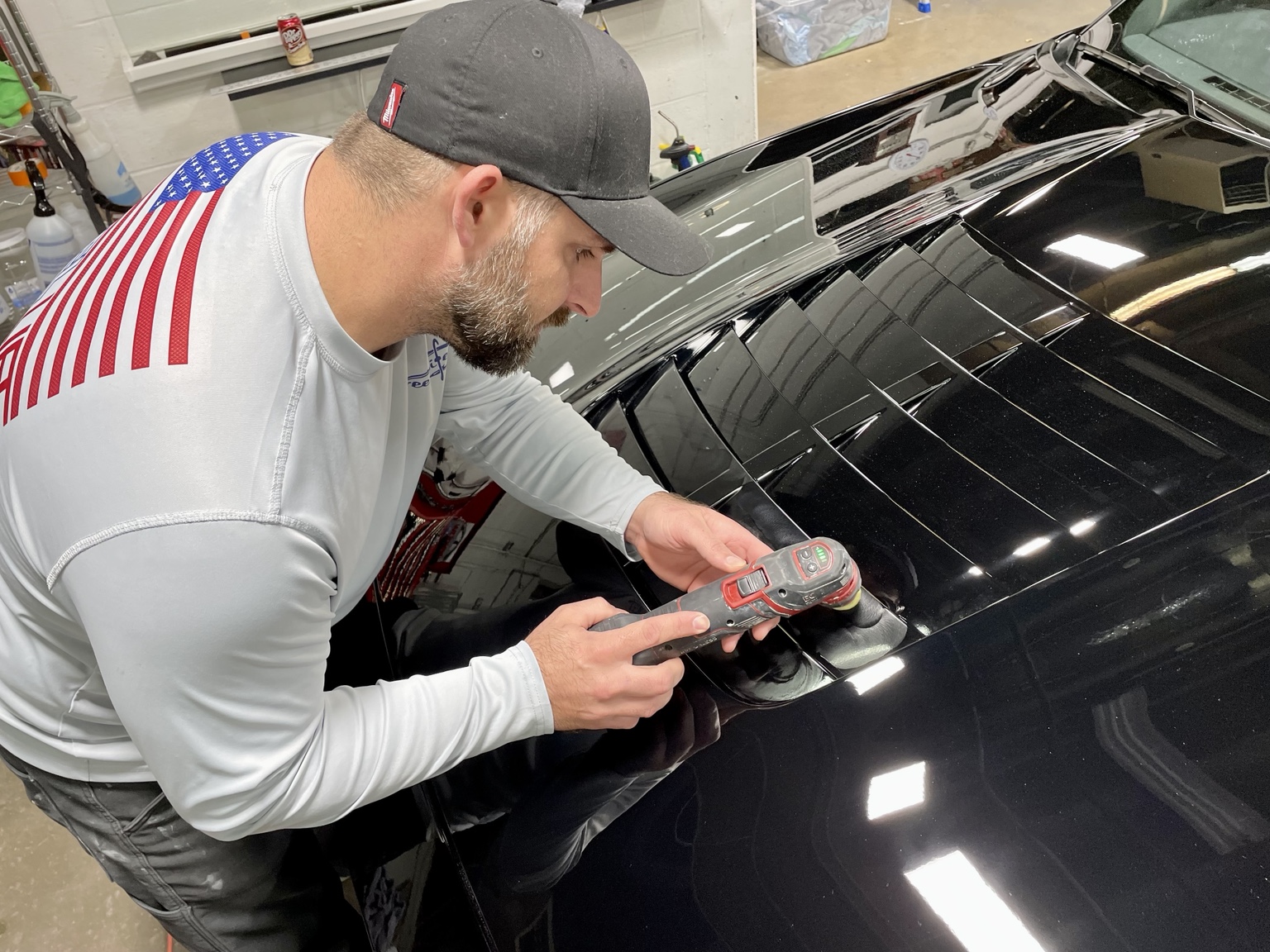 Owner machine-polishing a black Mustang hood under bright lights