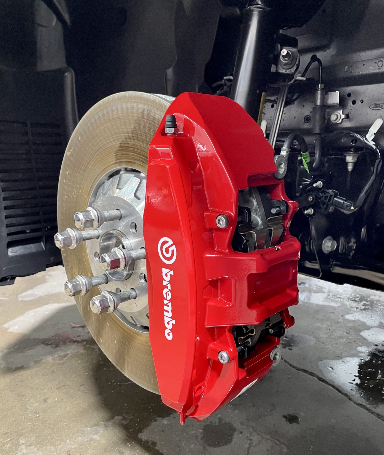 Wheel removed to expose a red Brembo brake caliper and brake rotor in the shop