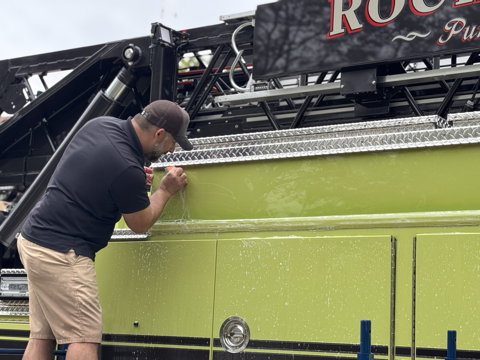 Close-up of hands-on paint protection film installation beneath the firetruck’s diamond-plate trim